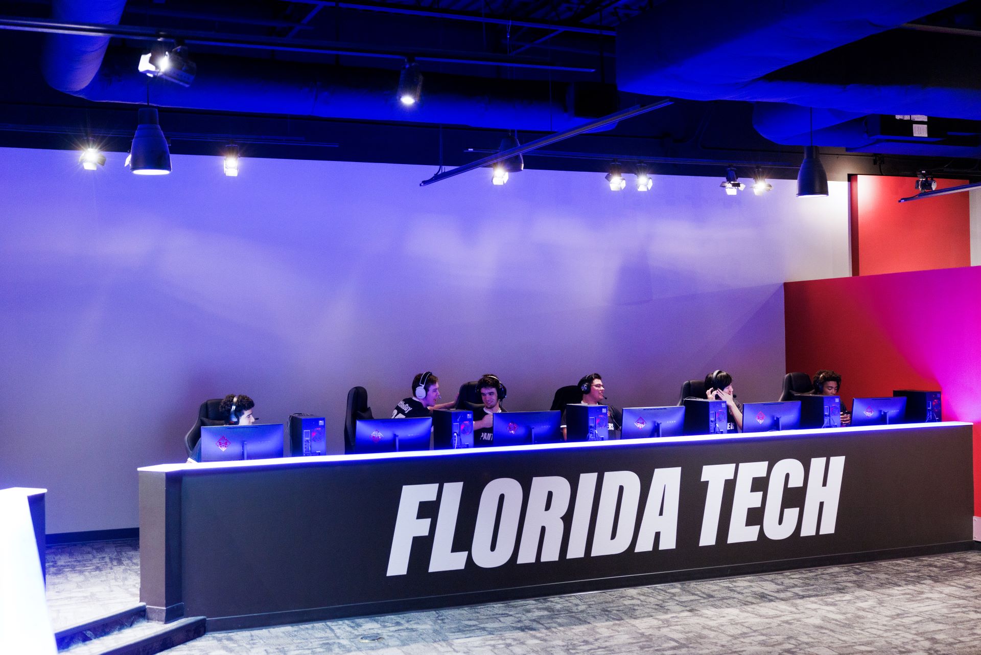Interior view of the Esports center with students seated at a row of computers, wearing headsets and playing games, with 'Florida Tech' prominently displayed on the front of the desk